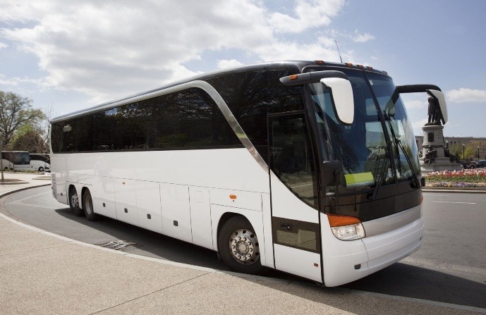 A large white tour bus parked on a street, showcasing its modern design and curved front. Ideal for group travel and sightseeing.
